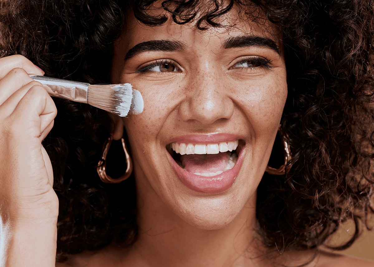 Girl smiling while applying makeup primer to face