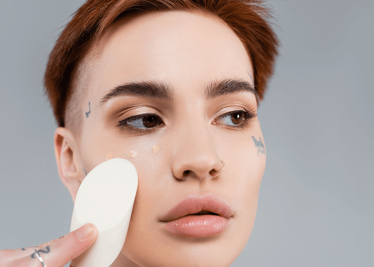 Tattooed woman applying makeup foundation with sponge