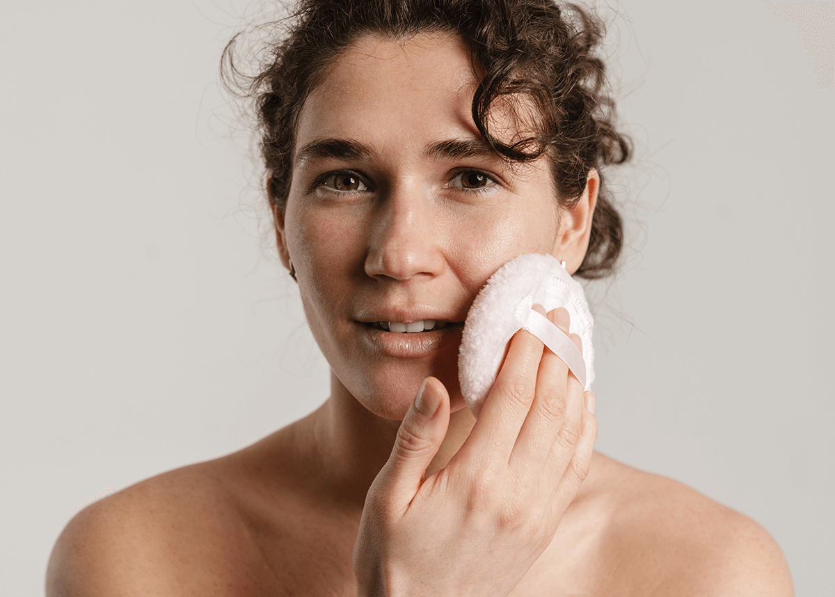 woman posing with powder sponge applying makeup to face