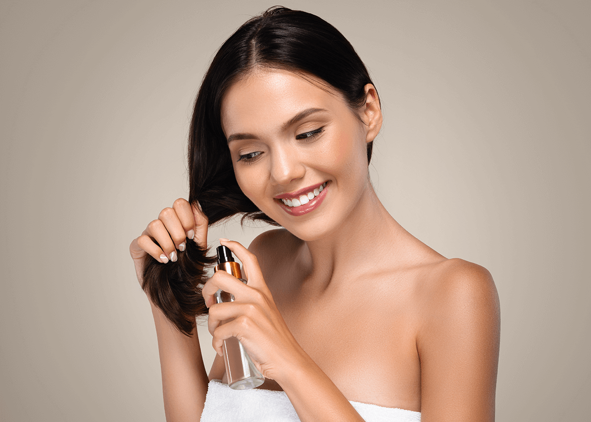 woman spraying product into hair to smell good